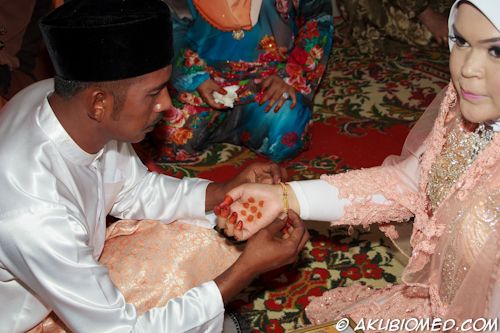 pengantin lelaki memasang rantai tangan kepada pengantin perempuan